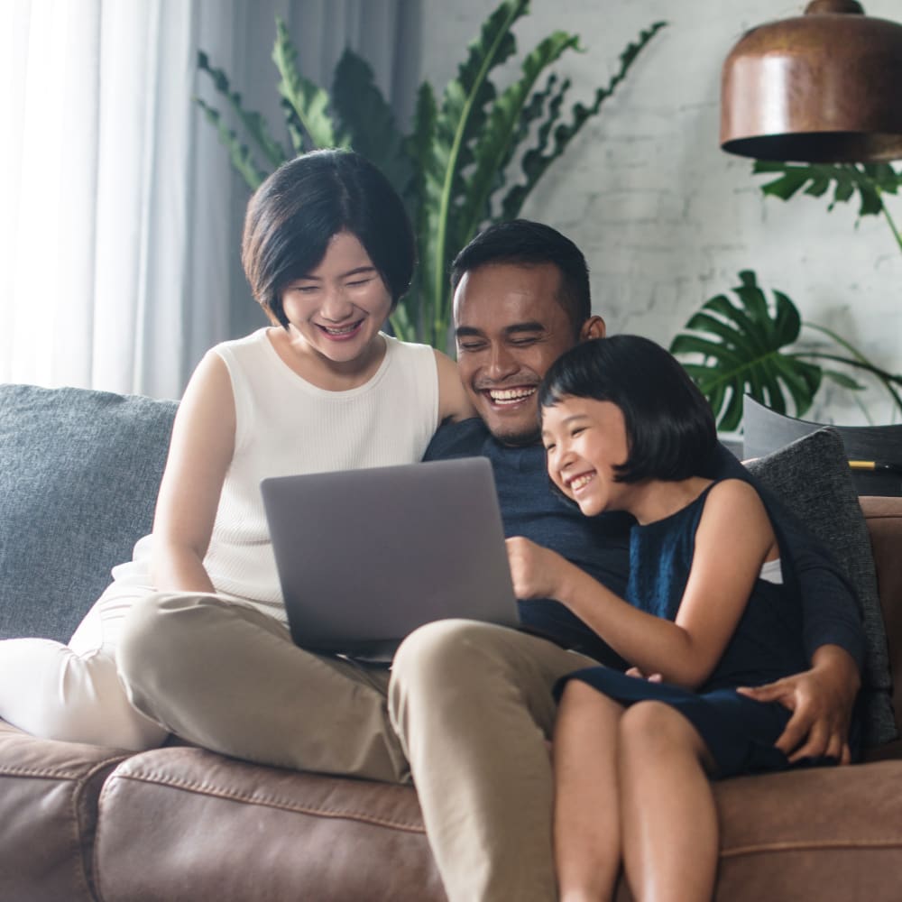 A diverse family is sitting together on a couch smiling and looking at a laptop.