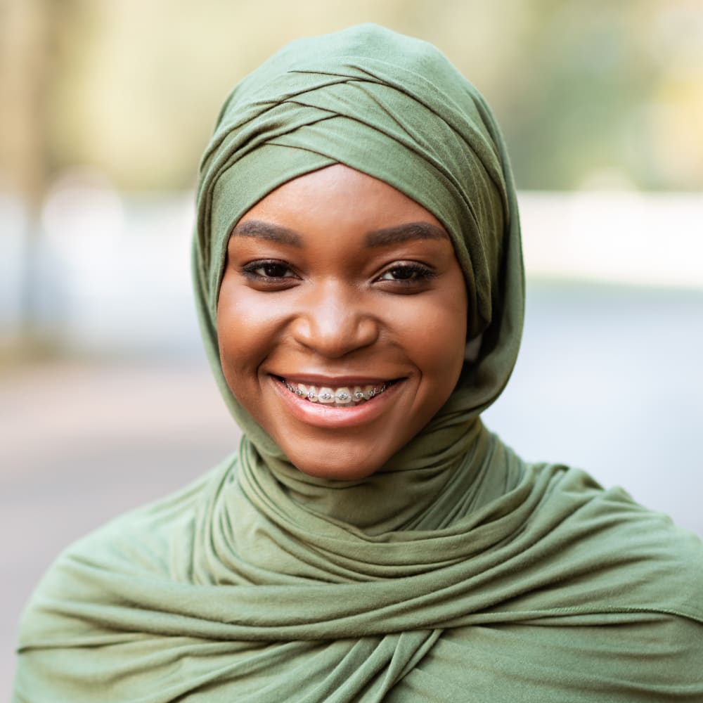 A woman with dark skin and a head scarf is smiling, revealing a mouth full of braces.
