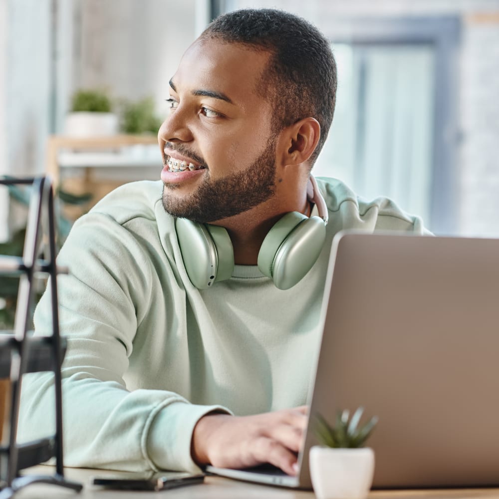 An adult man with braces is looking to the left. He is wearing a green sweatshirt that matches the headphones he has hanging around his neck.