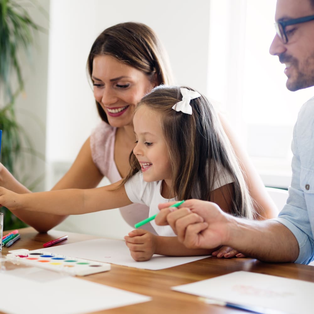 A young girl is sitting a table with her parents painting.