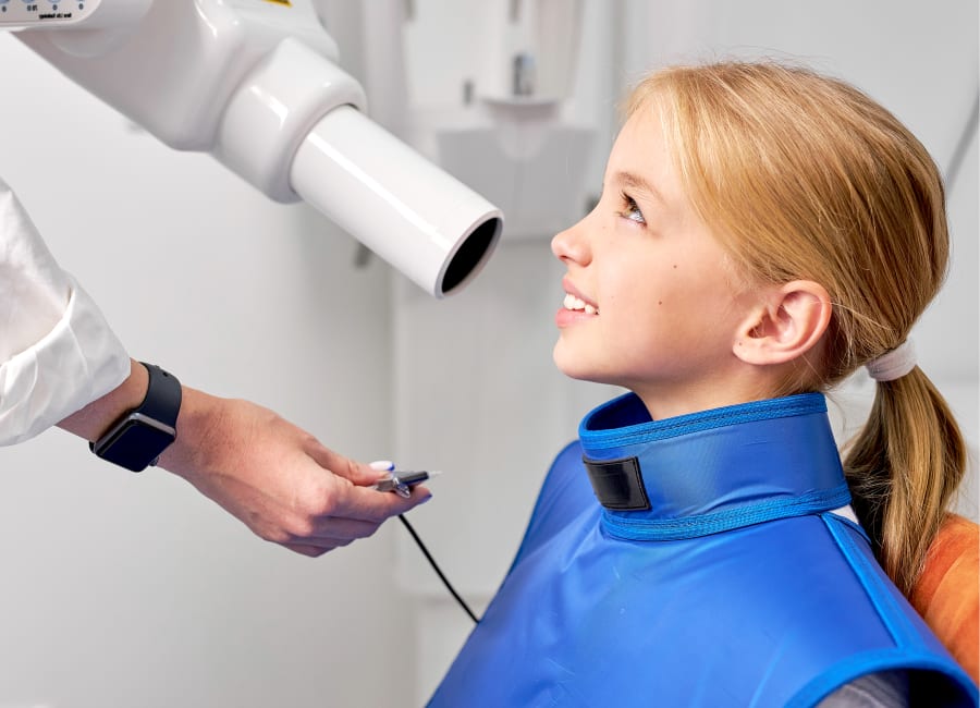 A young blonde girl prepares for a dental x-ray.
