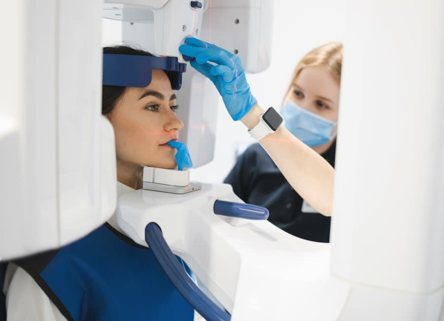 A woman with dark brown hair is sitting in a panoramic x-ray device.