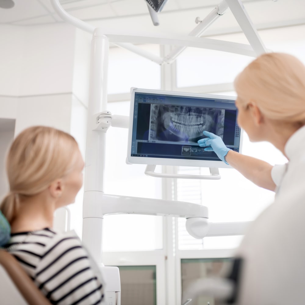 A blonde doctor shows a blonde patient a panoramic x-ray on a screen.
