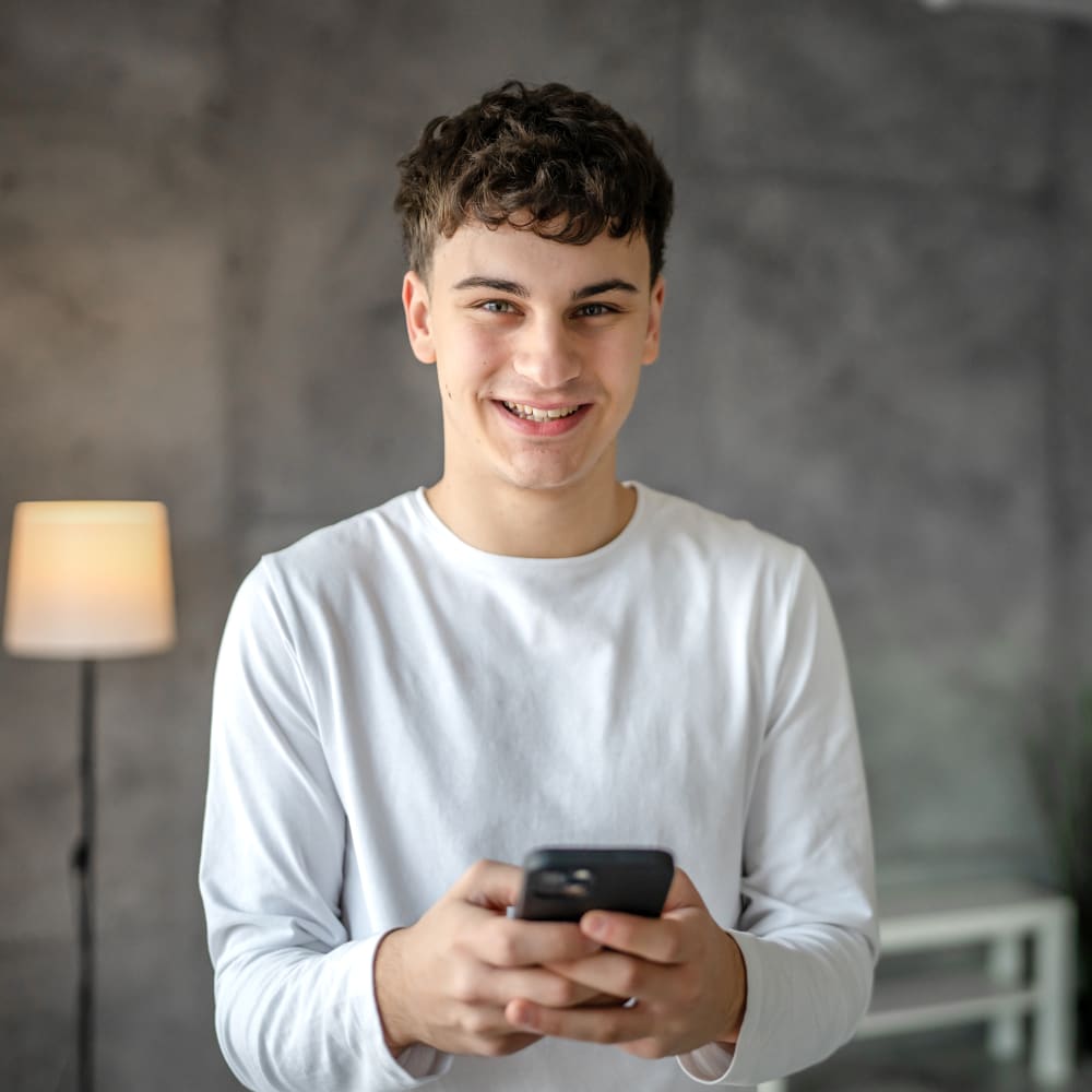 Teen boy smiles while typing on a smart phone.
