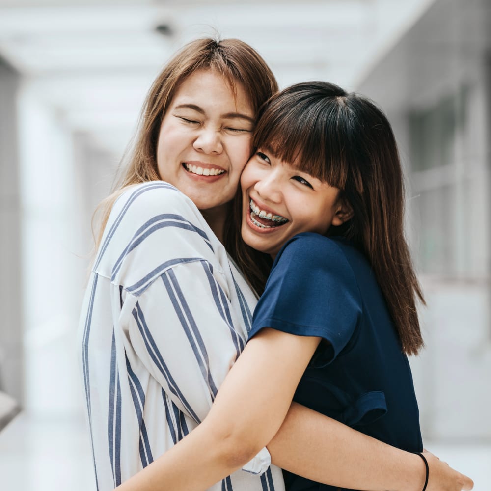 Two teenage girls are smiling and hugging. One of them has braces.
